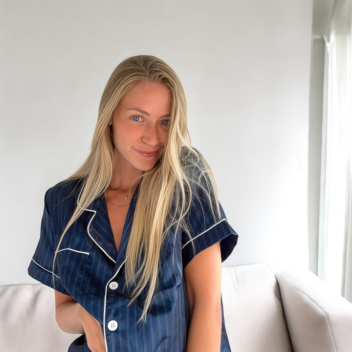Woman wearing navy striped satin short-sleeve pyjama top, seated indoors smiling | Grace Aura