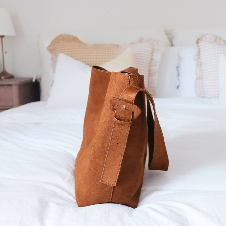 Cognac brown suede tote bag with strap, standing upright on bed | Grace Aura
