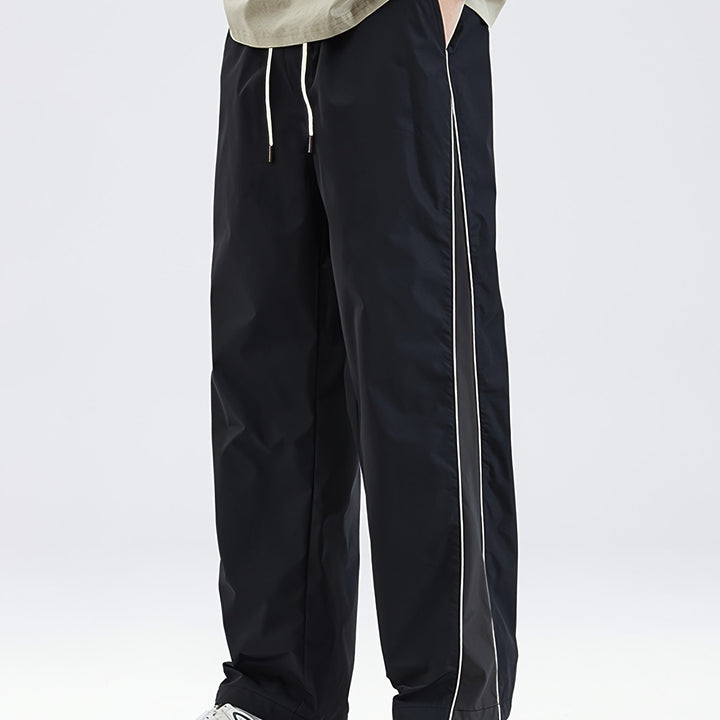 Black drawstring track pants with white side stripe, worn by person | Grace Aura