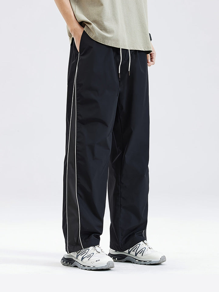 Black drawstring track pants with white piping, worn by man, sneakers | Grace Aura