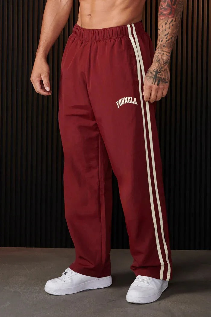 Maroon striped track pants with elastic waist worn by man standing | Grace Aura