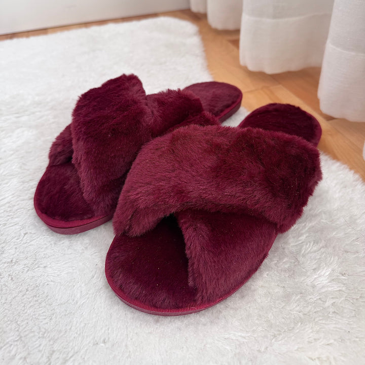 Burgundy fuzzy cross-strap slippers on white rug, flat lay view | Grace Aura