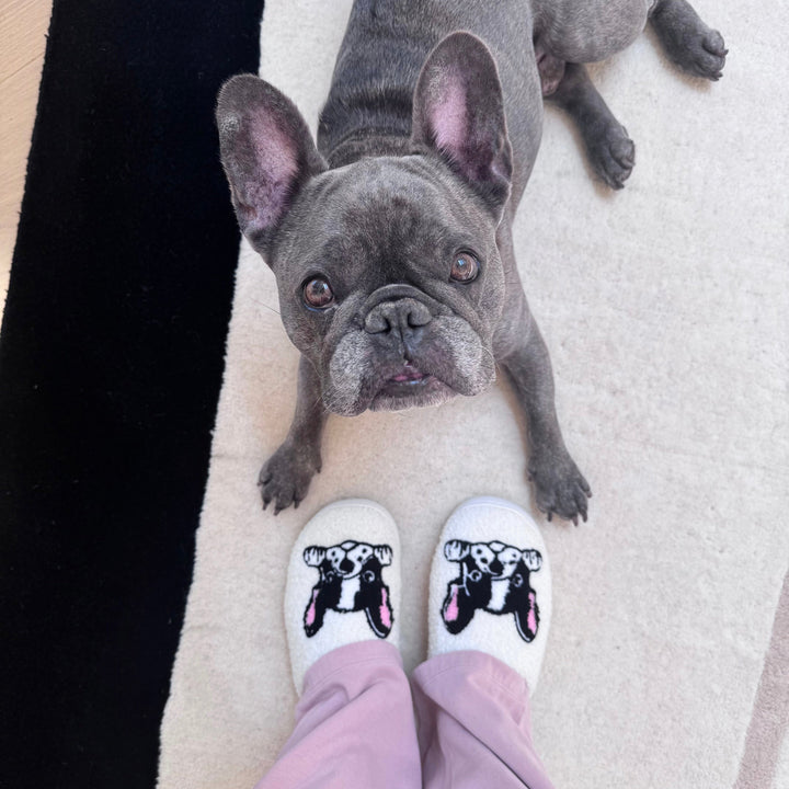 White plush slippers with dog print, worn by person, gray dog nearby | Grace Aura