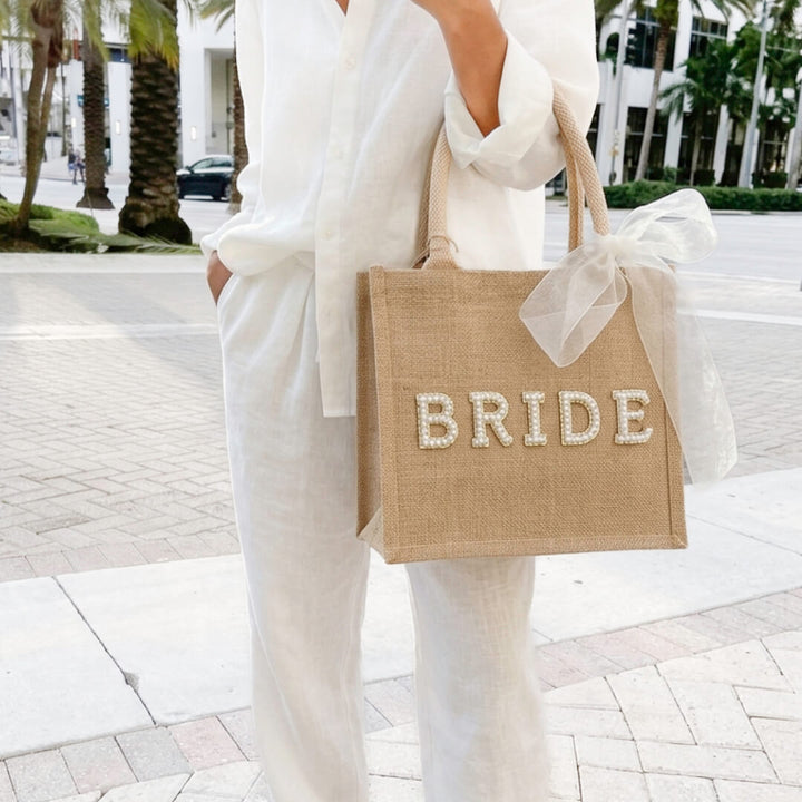 Woman carrying beige jute tote bag with pearl lettering, sheer bow | Grace Aura