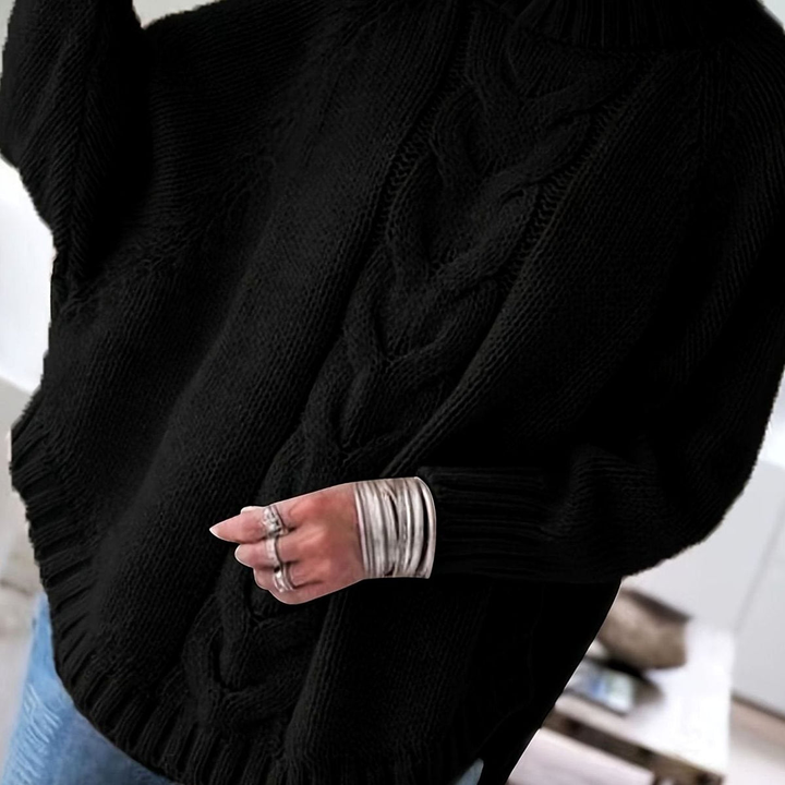 Close up side view of a person wearing an oversized black cable knit sweater with silver cuff bracelets and rings on one hand.