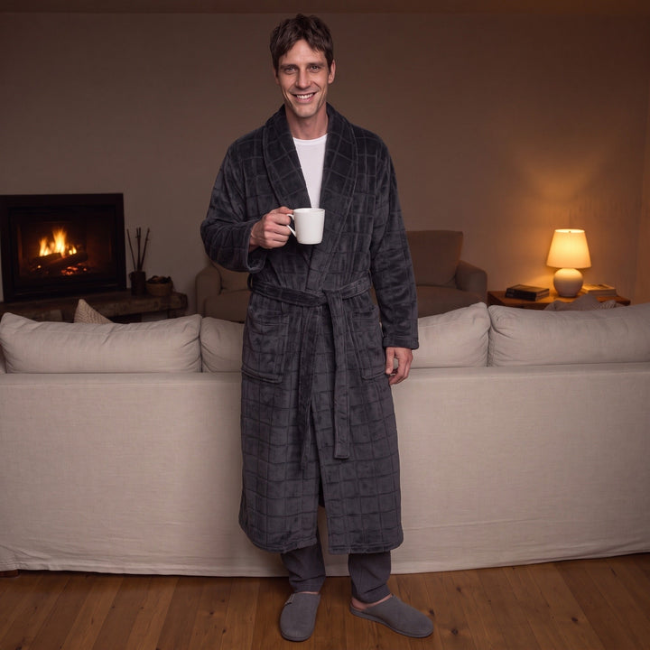 Man wearing dark grey checkered fleece dressing gown, holding mug, standing indoors | Grace Aura