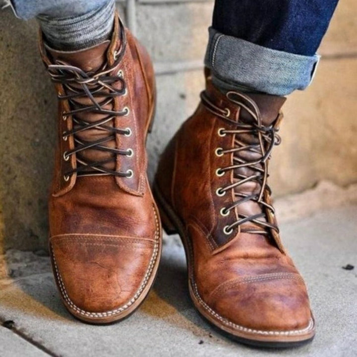 Brown lace-up leather cap-toe boots worn by person, cuffed jeans visible | Grace Aura