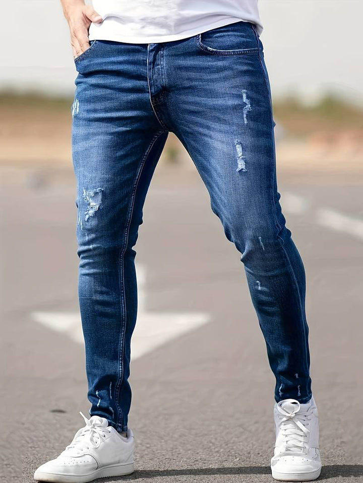 Man wearing dark blue distressed skinny jeans with white sneakers outdoors | Grace Aura