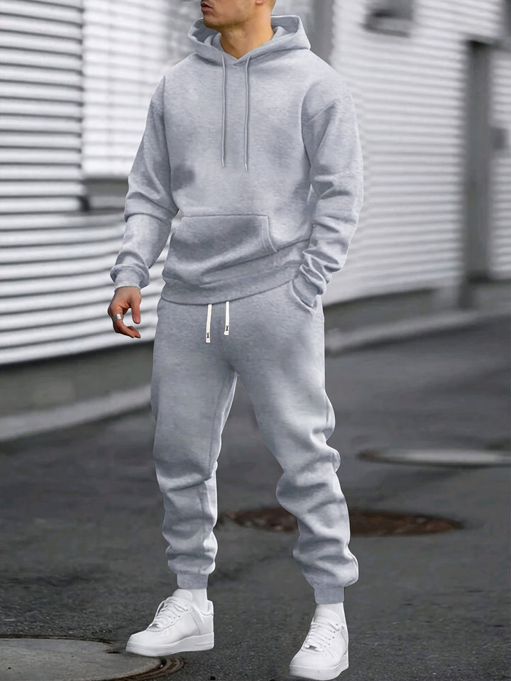 Man in a grey hoodie and matching joggers tracksuit set, standing on a street