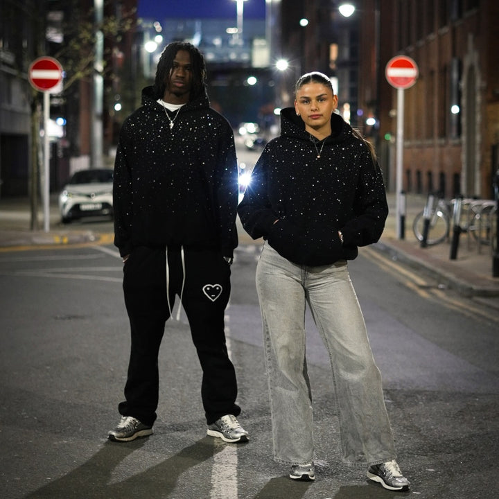 Black oversized rhinestone hoodie worn by a man and a woman on a city street at night
