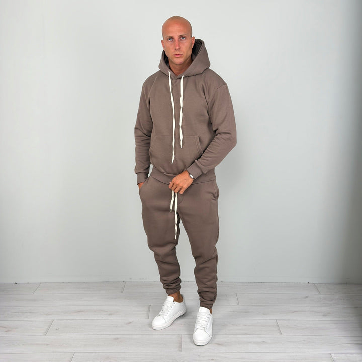 Man wearing brown hoodie tracksuit with joggers, worn, white sneakers, standing | Grace Aura