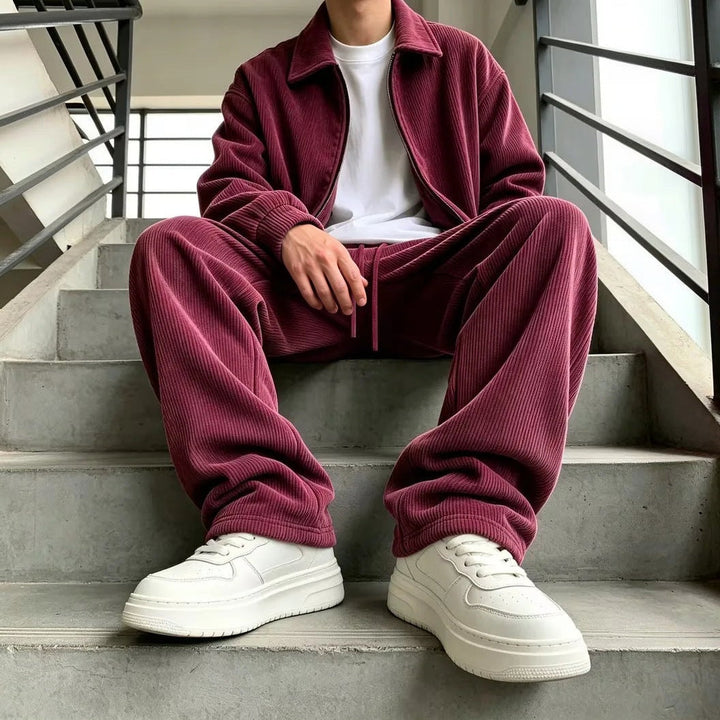 Man wearing burgundy corduroy zip jacket and wide trousers, seated on stairs | Grace Aura