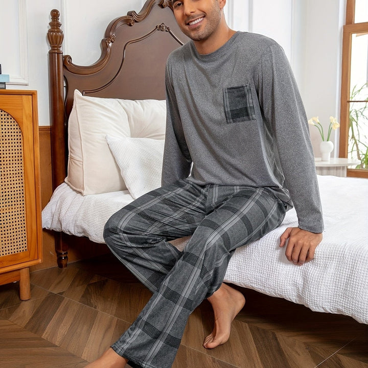 Man wearing grey top and plaid pyjama pants, seated on bed | Grace Aura