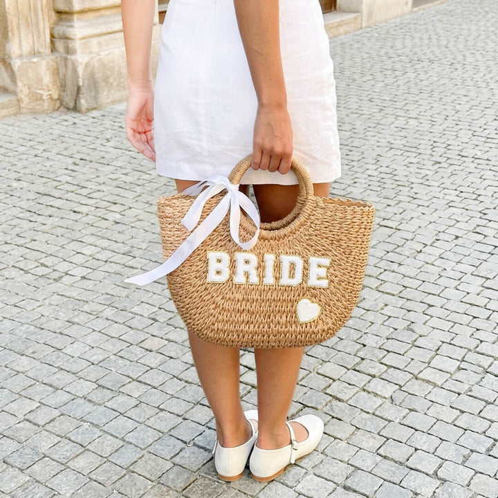 Woman carrying woven straw tote bag with white ribbon handle detail | Grace Aura