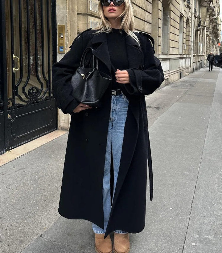 Long black trench coat worn open over jeans, with the belt hanging loose
