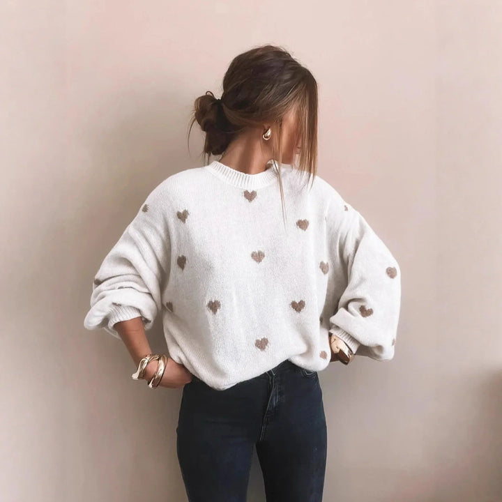 Women's white oversized jumper with knitted-in beige hearts, worn with dark jeans