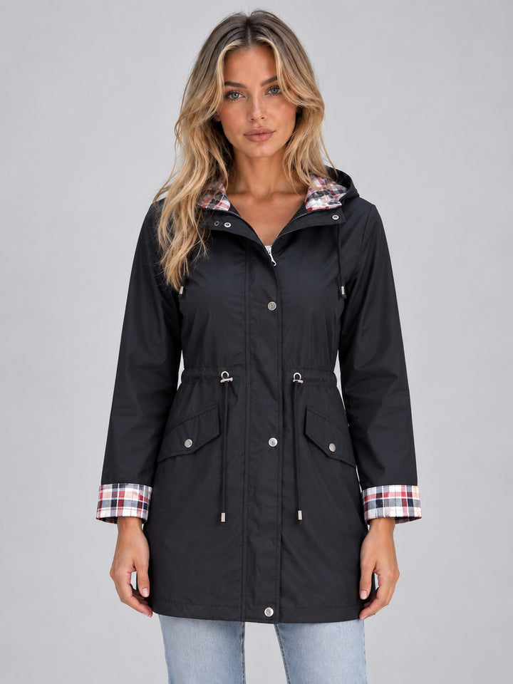 Woman wearing a long black raincoat with a check-lined hood, front