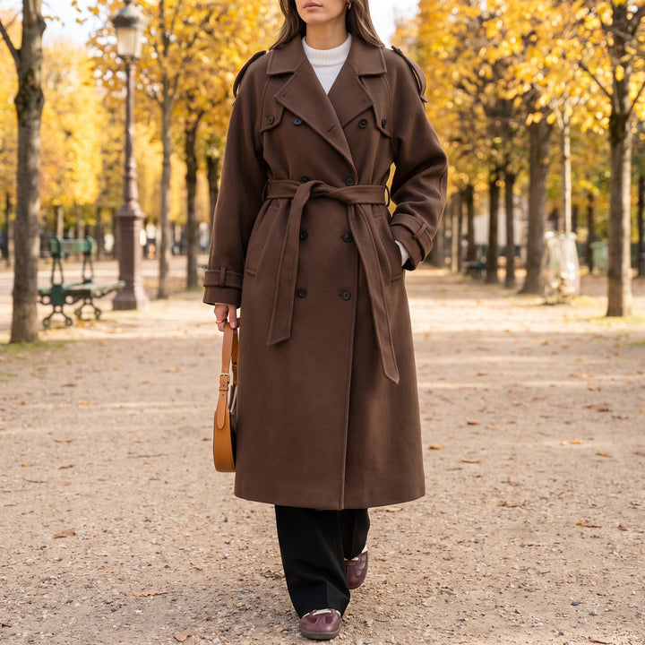 Brown long double-breasted coat with a tie belt, worn in a park