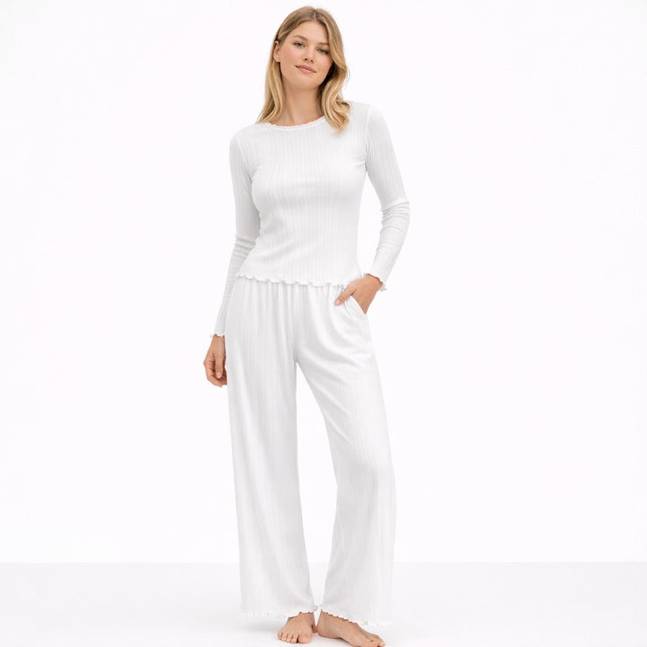 Woman wearing a white pointelle pyjama set with a long-sleeve top and wide-leg trousers